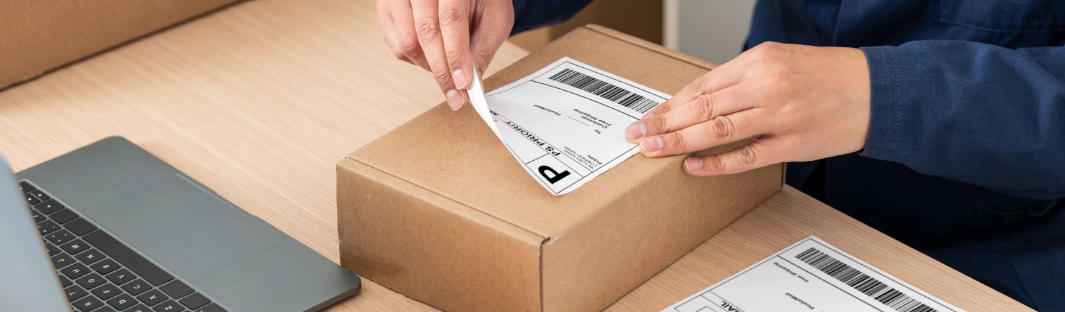 Pracownik nakleja etykietę z kodem kreskowym wydrukowaną w HDF Labels na paczkę logistyczną